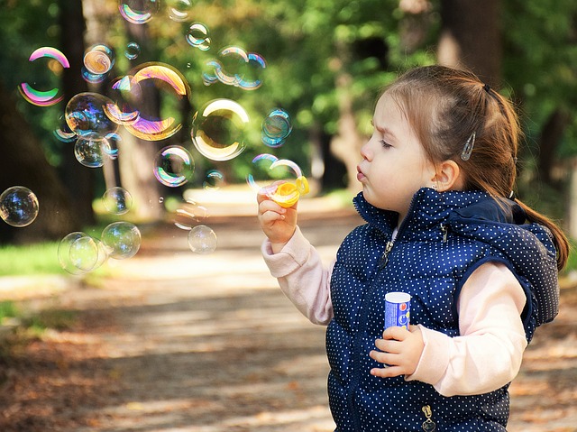 Ein kleines Mädchen steht im Wald und bläst Seifenblasen