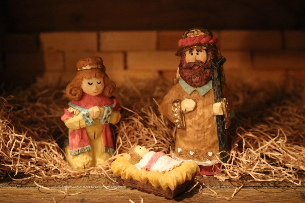 Figuren aus Modelliermasse: Jesus als Baby in der Krippe, Maria und Josef. Am Boden Stroh, hinten: Ziegelmauer.